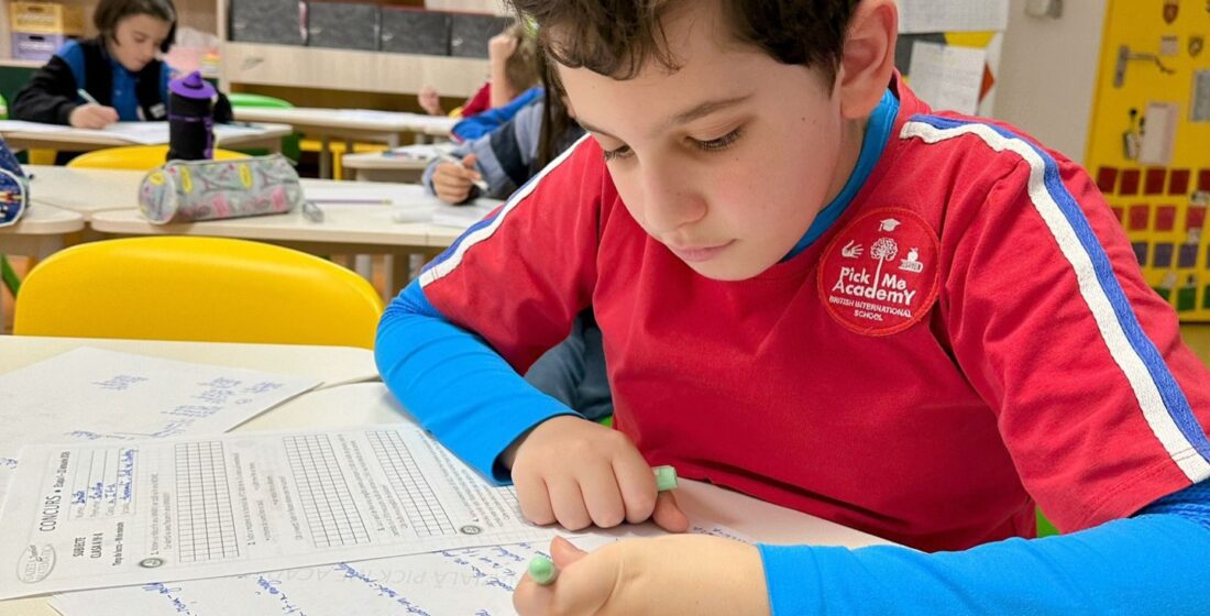 Un elev scriind temele pe hârtie, dezvoltându-și capacitatea de concentrare, fără un telefon mobil pe birou.