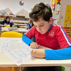 Un elev scriind temele pe hârtie, dezvoltându-și capacitatea de concentrare, fără un telefon mobil pe birou.