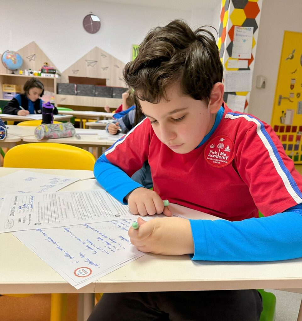 Un elev scriind temele pe hârtie, dezvoltându-și capacitatea de concentrare, fără un telefon mobil pe birou.